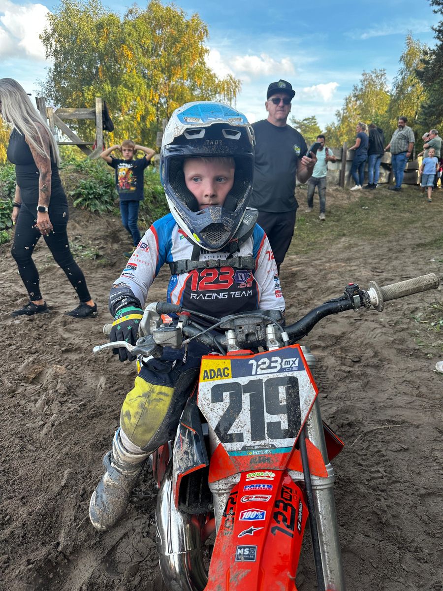 Ein kleiner Fahrer im 123MX-Racing-Team-Trikot mit offenem Helm sitzt auf seinem Motorrad mit der Startnummer 219
