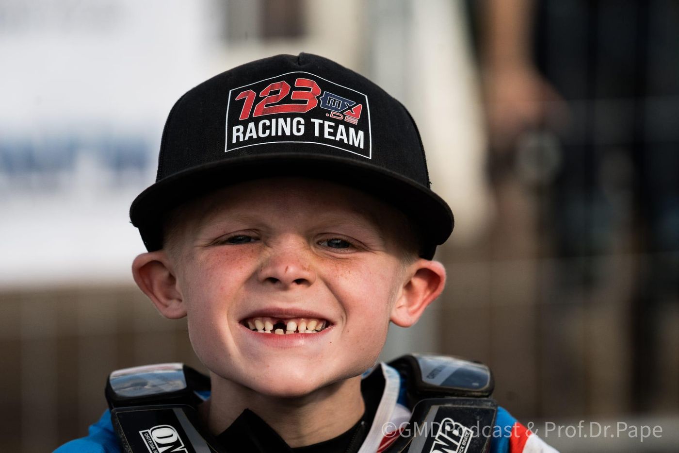Ein lachender Junge mit Zahnlücke trägt eine schwarze Kappe mit der Aufschrift 123MX Racing Team