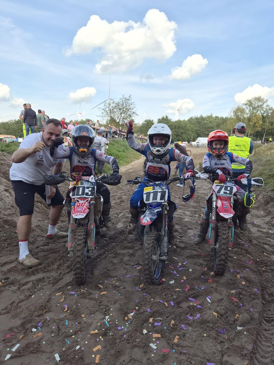 Drei junge Fahrer mit den Startnummern 103, 111 und 79 jubeln auf ihren Motorrädern im Sand voller Konfetti, daneben ein Betreuer im 123MX-Shirt