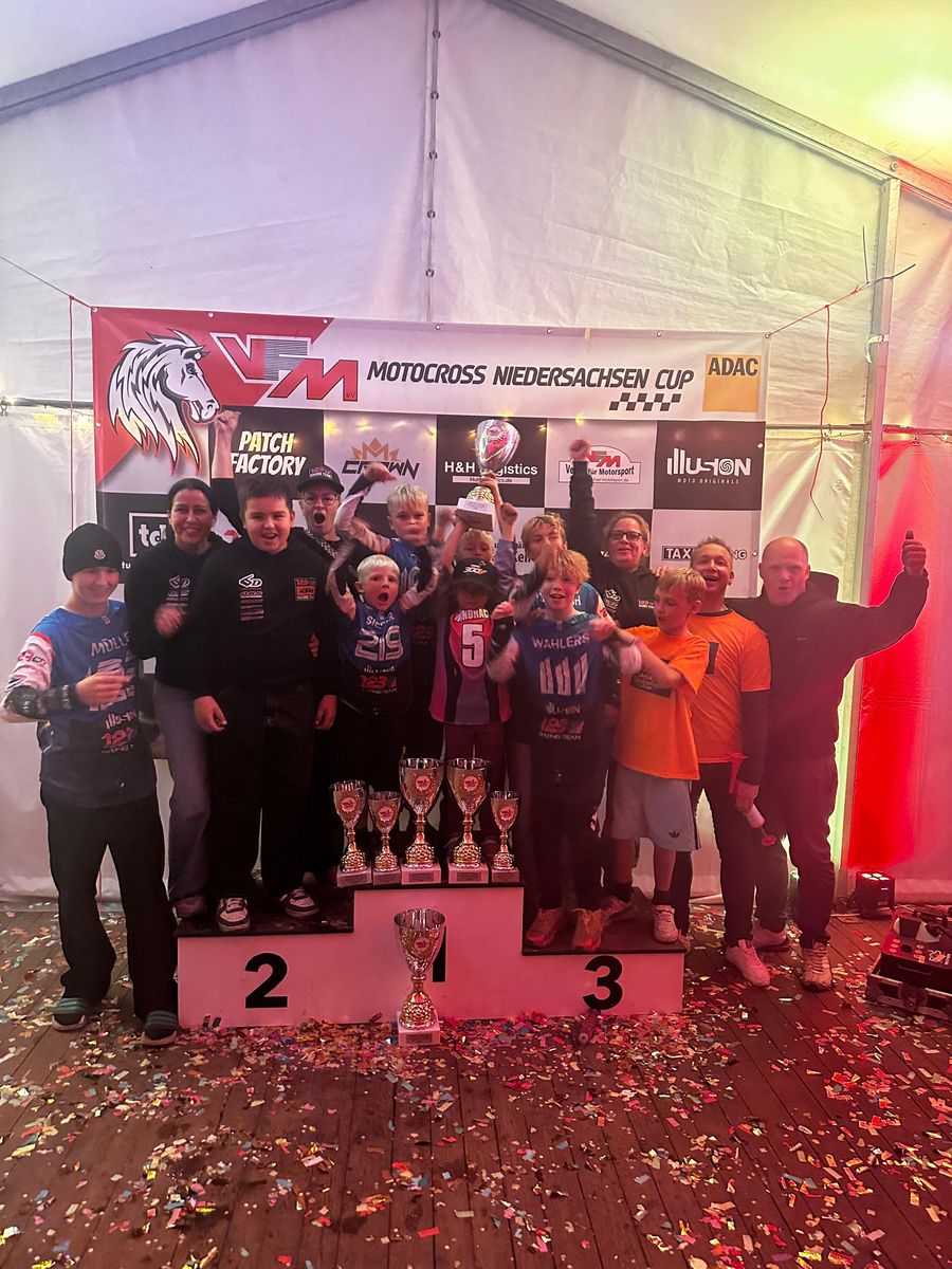 Fahrer, Eltern und Betreuer des 123MX Racing Teams jubeln auf dem Siegerpodest vor dem Banner des VFM Motocross Niedersachsen Cup, ein Fahrer hält einen großen Pokal hoch