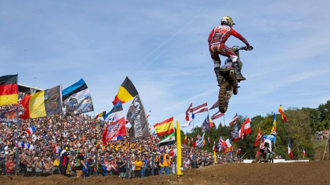 Karlis Reisulis im Sprung vor den Fahnen der Nationen beim Motocross of Nations 2026 in Ernée