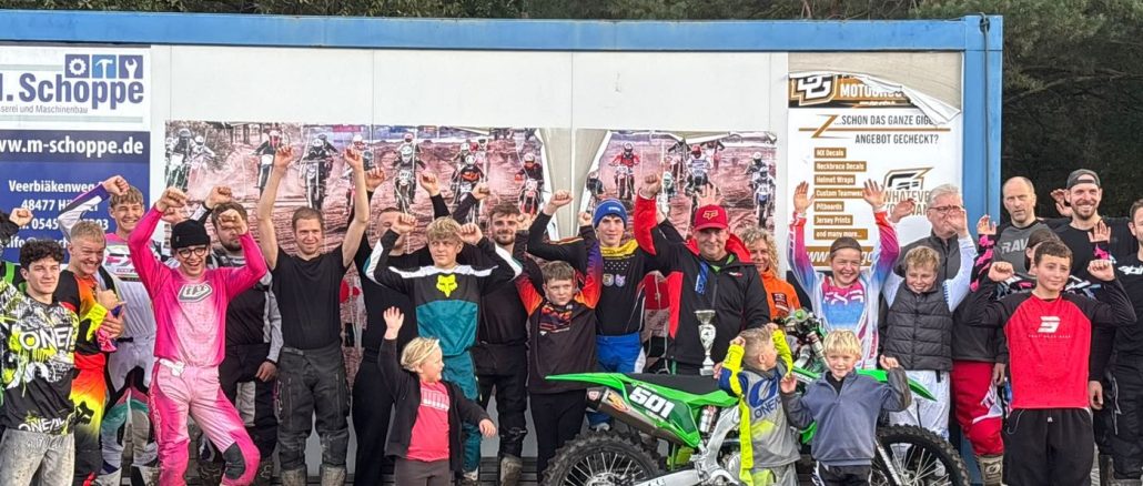 Lehrgangsteilnehmer jubeln mit erhobenen Armen hinter Dirk Pohls grüner Kawasaki mit der Startnummer 501 und einem Pokal
