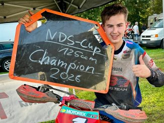 Mio Müller hält eine Tafel mit der Aufschrift NDS-Cup 125ccm Champion 2026 und zeigt den Daumen nach oben, vor ihm sein Motorrad mit der Startnummer 1