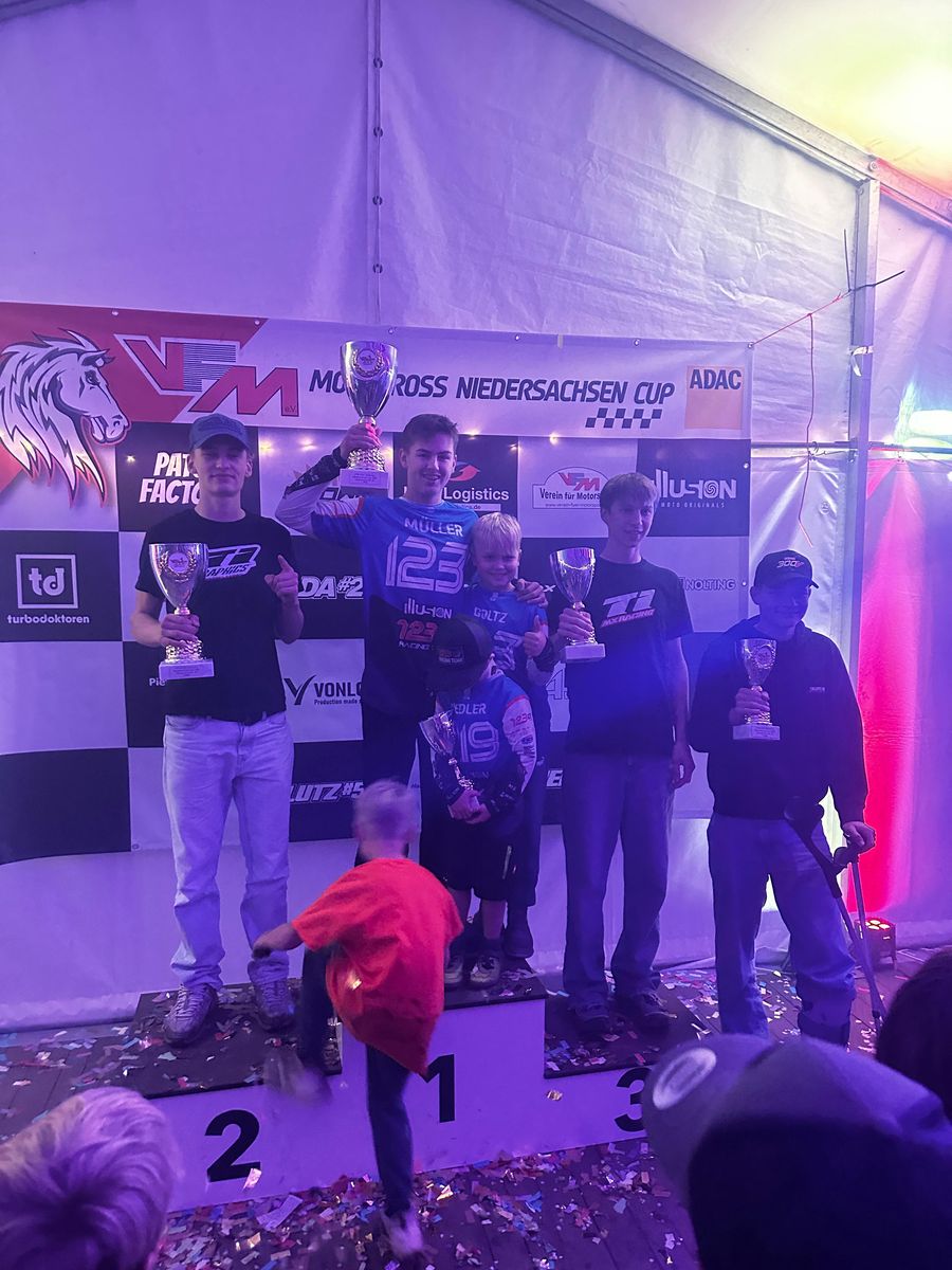 Mio Müller mit der Startnummer 123 steht in der Mitte des Podests und stemmt einen Pokal, links und rechts die Platzierten mit ihren Pokalen
